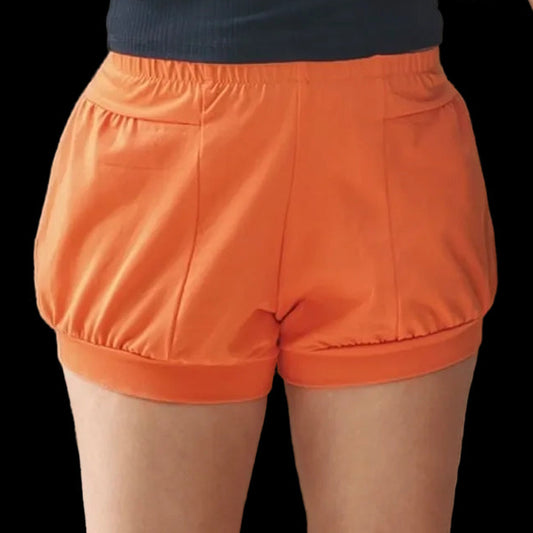 A person wearing bright orange iyengar yoga shorts with a gathered elastic waistband, paired with a dark ribbed top.