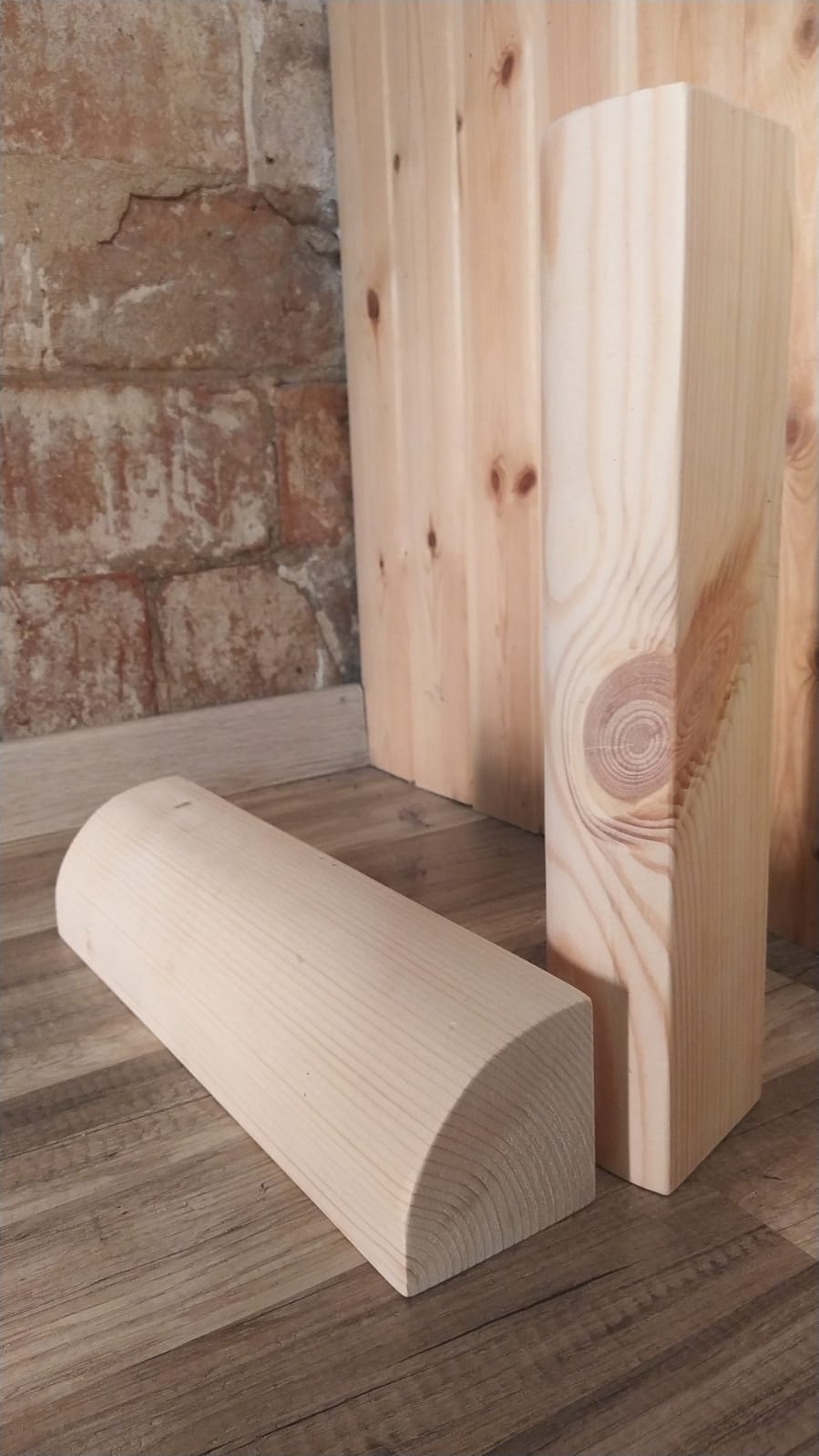 Two wooden iyengar quarter round wood blocks on a wooden floor with a brick wall background