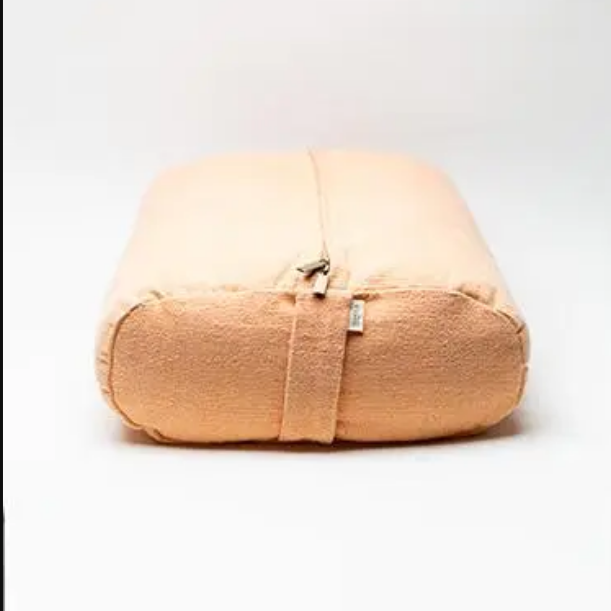 A peach-colored fabric yoga bolster with a zippered top and a horizontal strap closure, shown on a clean white background.