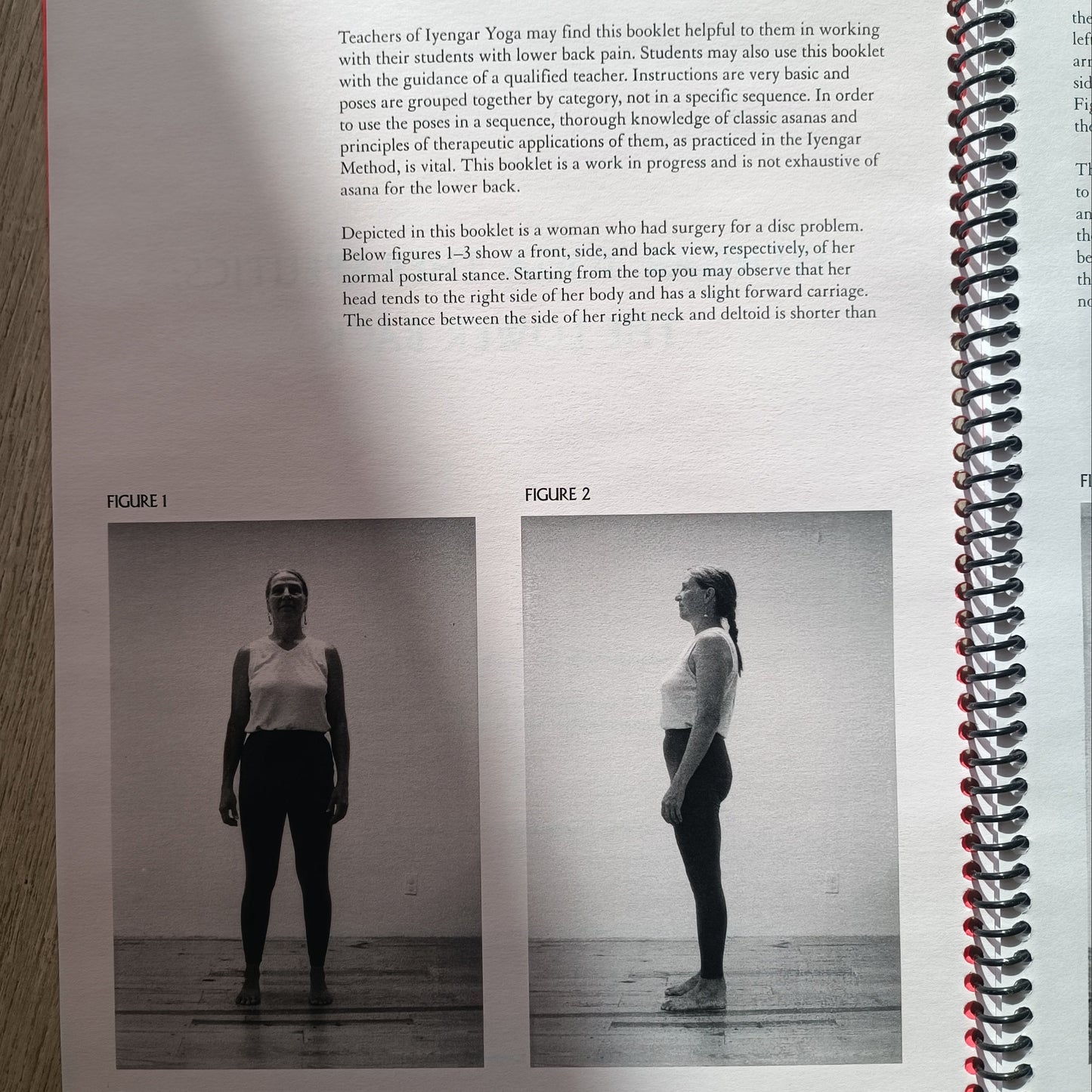 An open spiral-bound book or magazine lying on a light wood surface, showing a black-and-white photo of a person standing upside down on a board, with text below and a red page marker visible.