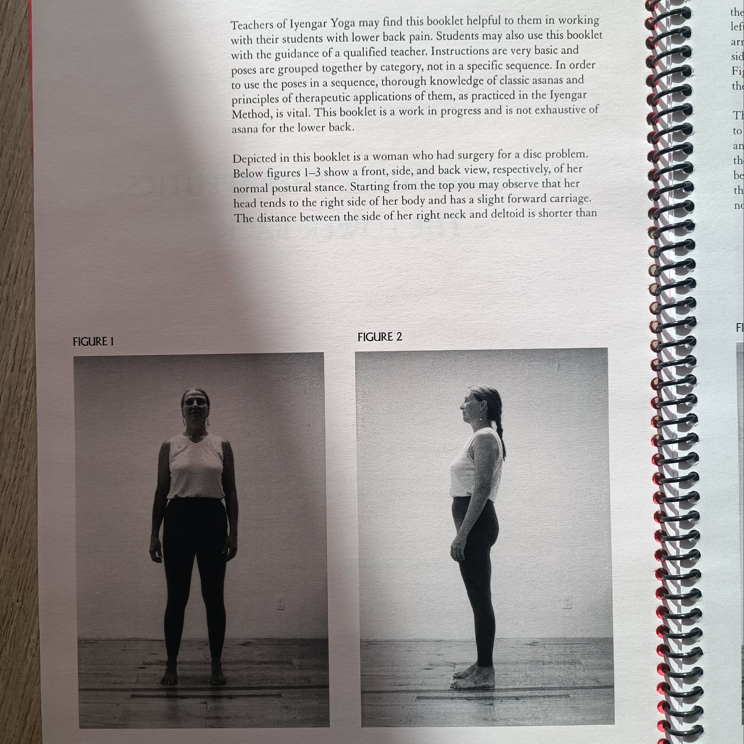 An open spiral-bound book or magazine lying on a light wood surface, showing a black-and-white photo of a person standing upside down on a board, with text below and a red page marker visible.
