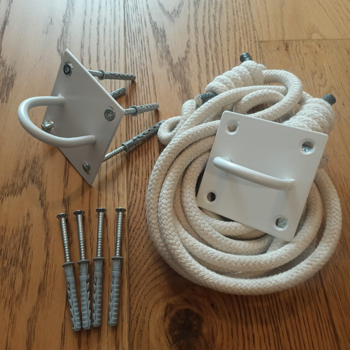 white yoga ropes set with two white metal mounting brackets, four silver wall anchors, and screws, arranged on a wooden floor.