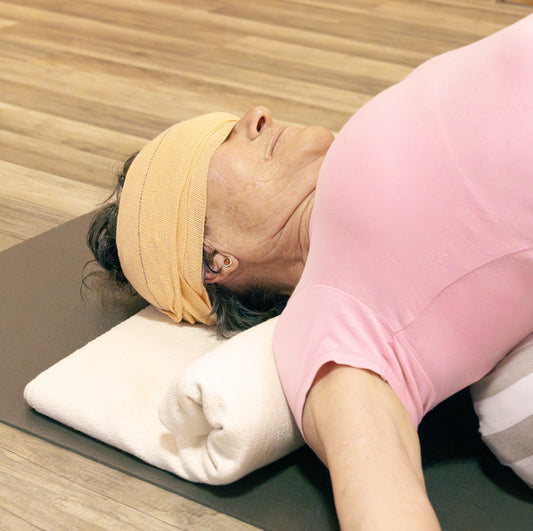 Person lying on a yoga mat with a yoga headwrap and pink top, in a yoga pose.