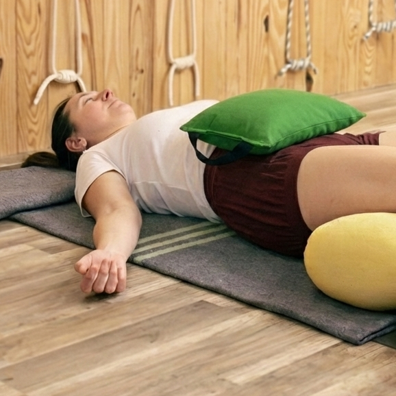 Person lying on a mat with yoga bolsters under legs and a sandbag on the belly