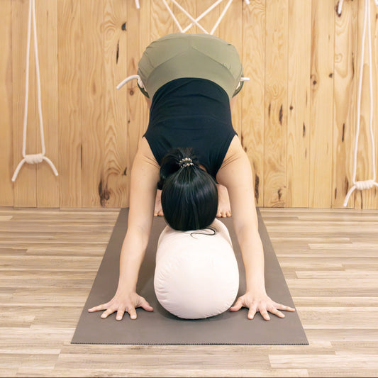 Person practicing iyengar yoga wearing comfortable pune shorts with a beige bolster on a wooden floor.