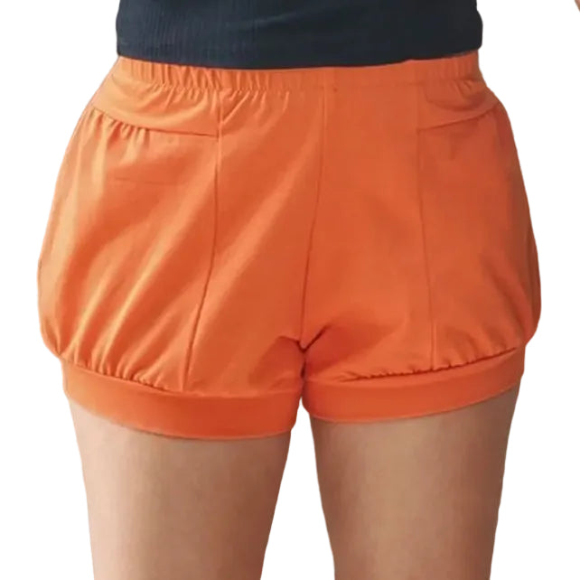 A person wearing bright orange iyengar yoga shorts with a gathered elastic waistband, paired with a dark ribbed top.