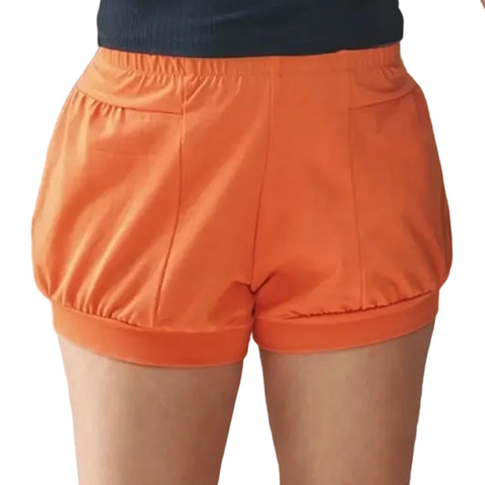 A person wearing bright orange iyengar yoga shorts with a gathered elastic waistband, paired with a dark ribbed top.