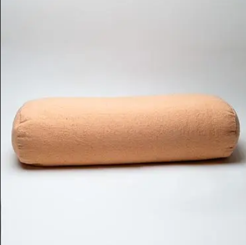 A cylindrical yoga bolster pillow in a light peach-beige color, shown against a plain light gray background.