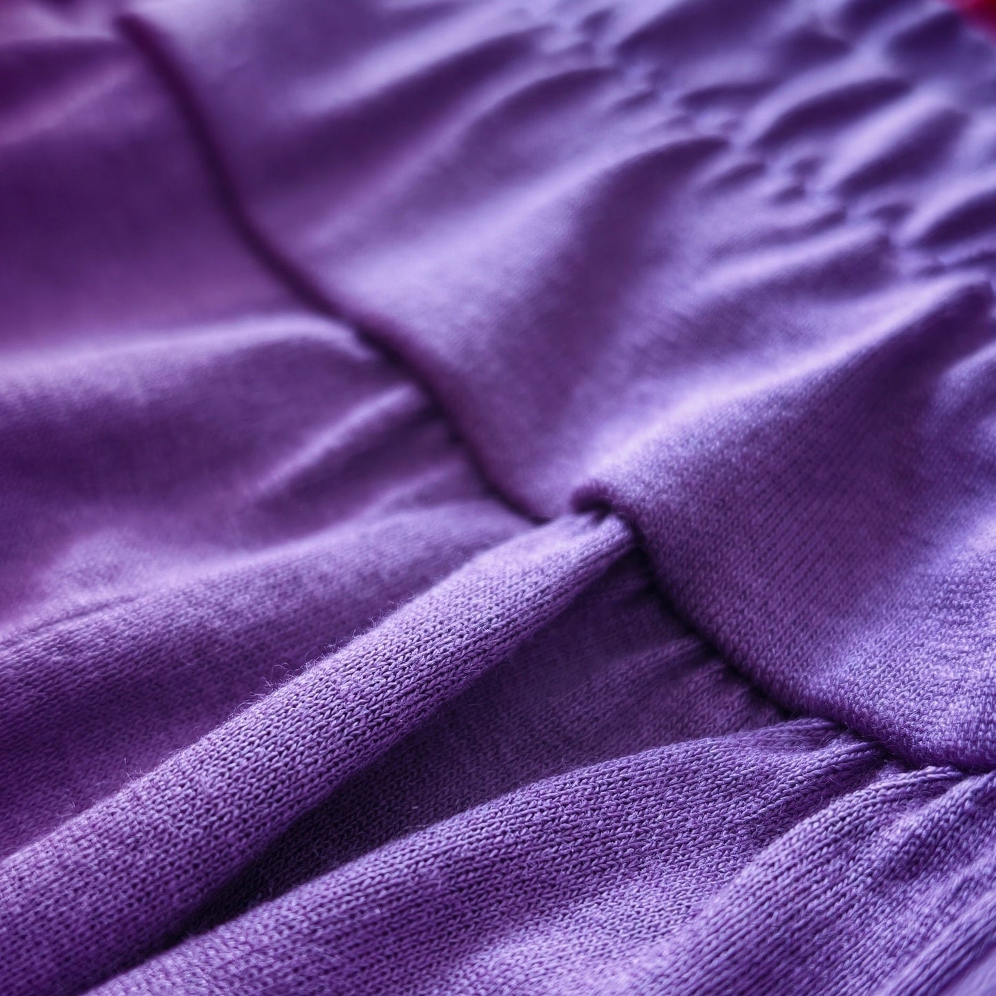 Close-up of a purple textured fabric with gathered pleats and a red striped trim along the edge.