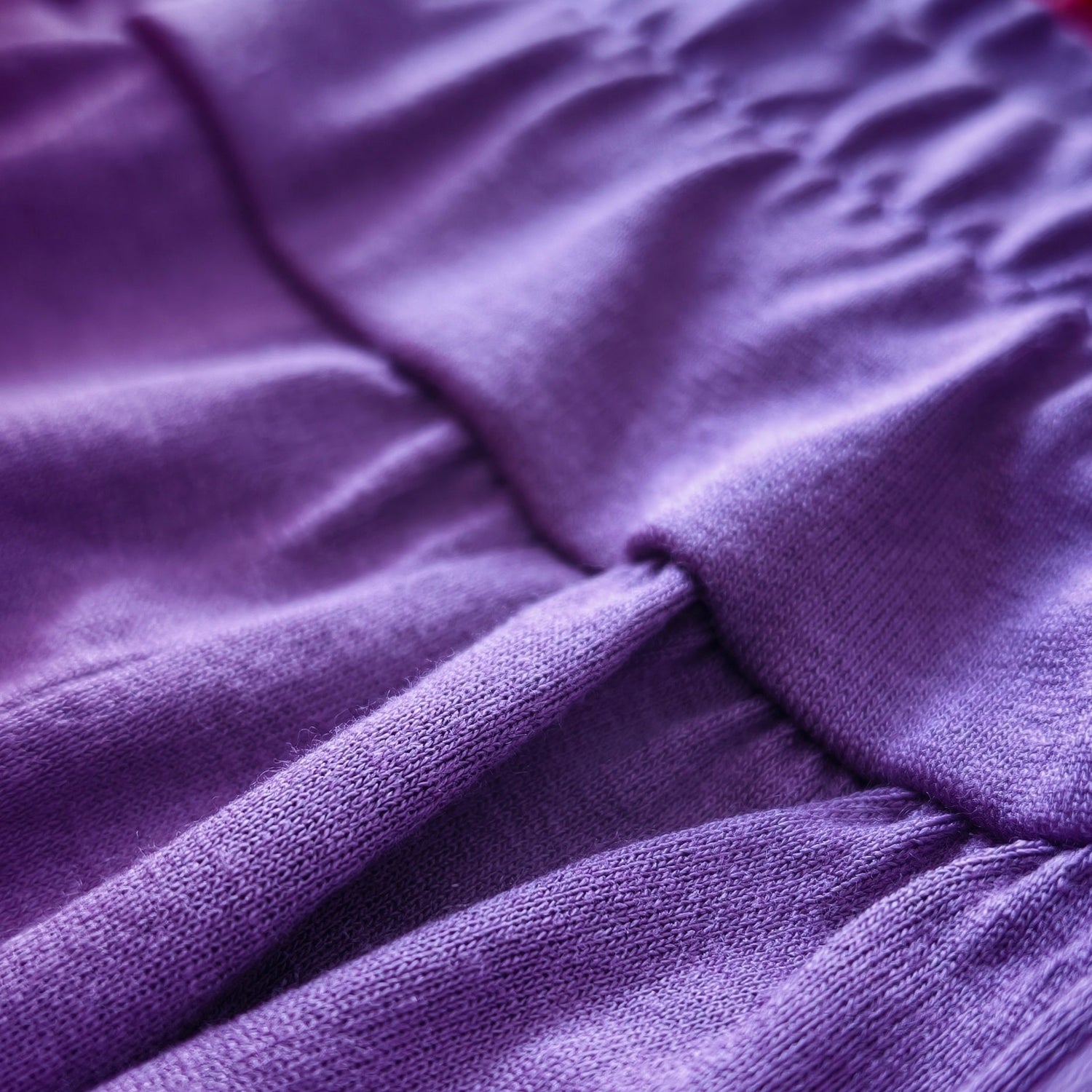 Close-up of a purple textured fabric with gathered pleats and a red striped trim along the edge.