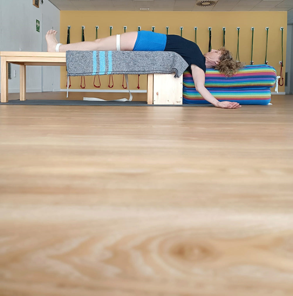 Person lying on a yoga bench with colorful yoga bolsters and blanket