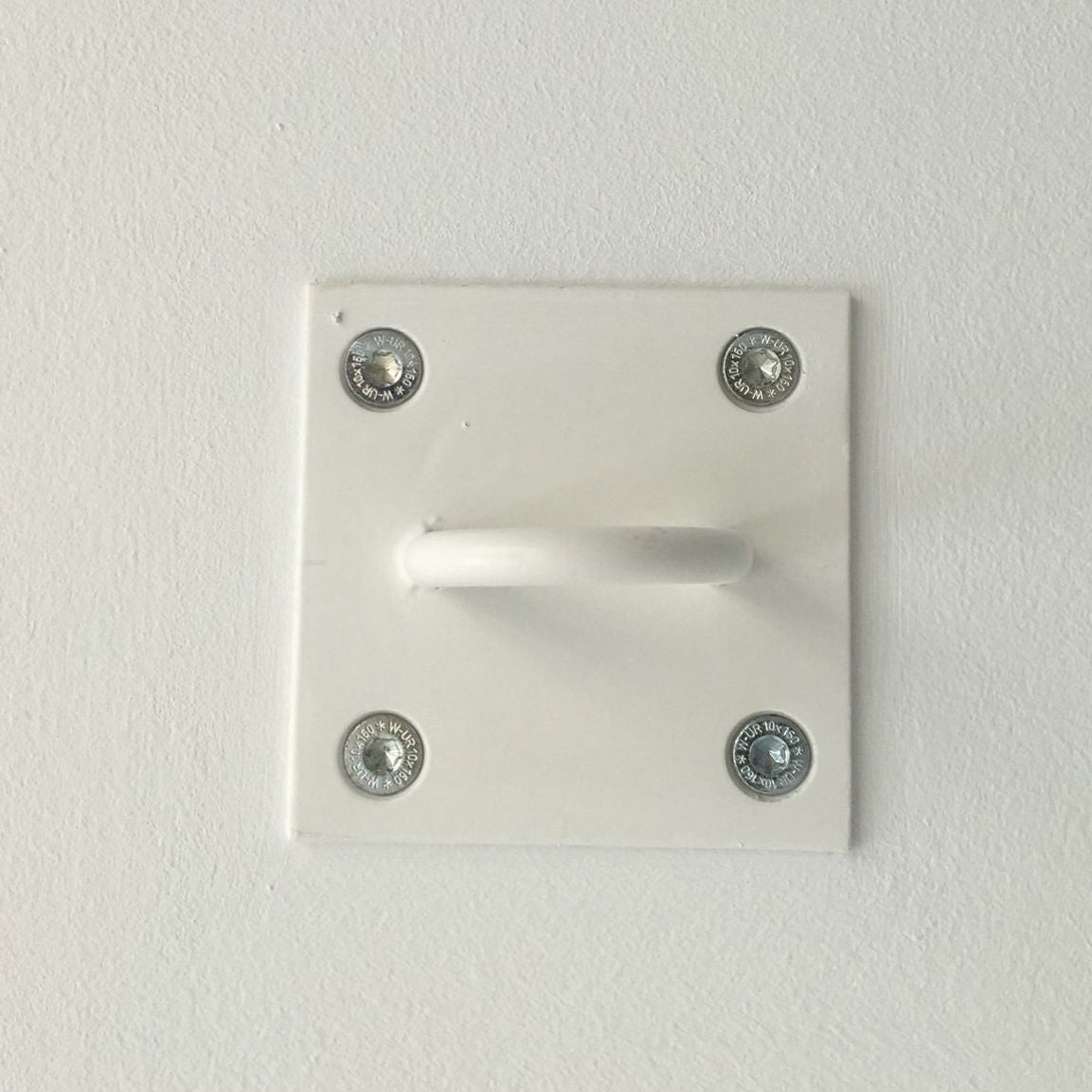 A white wall-mounted hook with a square backplate secured by four silver screws, shown against a plain white textured wall.